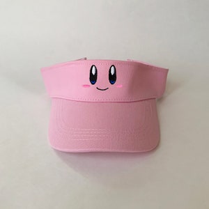 May include: Pink visor with an embroidered pink and blue Kirby character face.