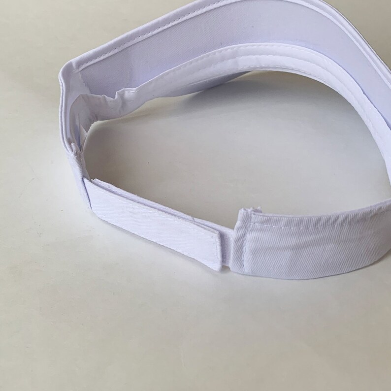 Op de afbeelding: Een witte visor met een verstelbare band aan de achterkant. De visor is gemaakt van een zachte, ademende stof.
