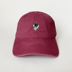 Puede incluir: Una gorra de b&eacute;isbol de color burdeos con un border collie blanco y negro bordado en la parte delantera.
