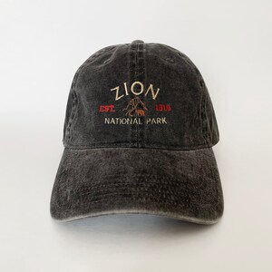 May include: A black distressed baseball cap with an embroidered logo that reads "Zion National Park Est. 1919".