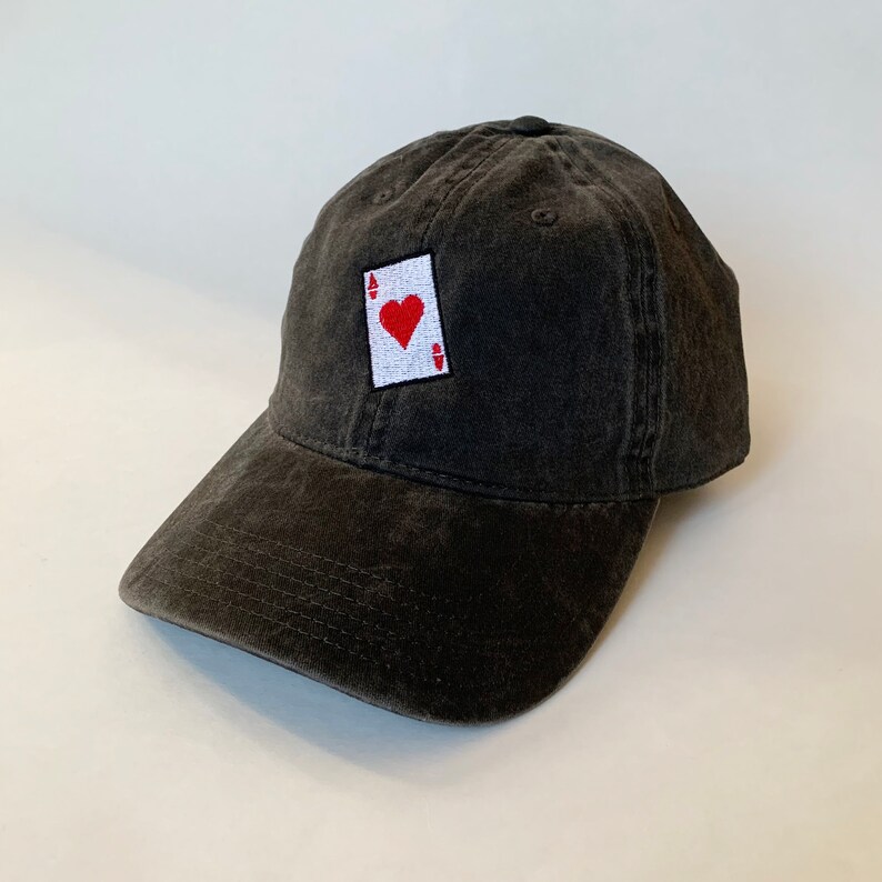 以下が含まれることがあります： 前面に赤いハートのエースのトランプが刺繍された黒い野球帽
