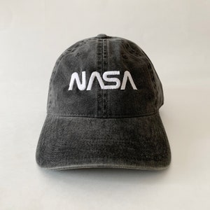 May include: A black, distressed, cotton baseball cap with a white embroidered NASA logo.