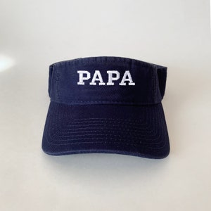 May include: A navy blue visor with white embroidered text that reads "PAPA".