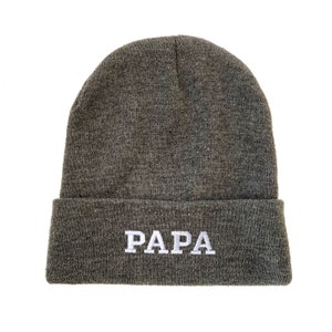 May include: Gray knitted beanie with a white embroidered word "PAPA" on the front.