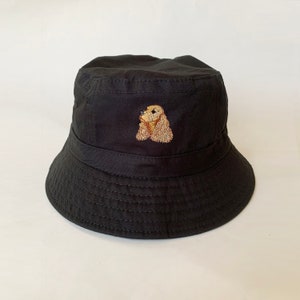 May include: A black bucket hat with an embroidered image of a brown and white cocker spaniel.
