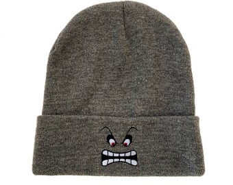 May include: Gray knitted beanie with a white embroidered angry face with red eyes.