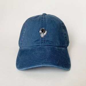 Puede incluir: Una gorra de b&eacute;isbol de mezclilla azul con un perro border collie blanco y negro bordado en la parte delantera.