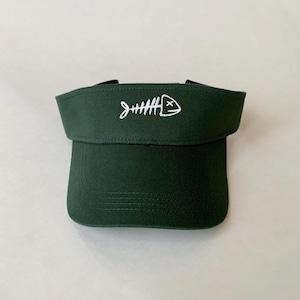 May include: A dark green visor with a white embroidered fish skeleton design. The fish skeleton has a cross for eyes.