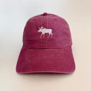 May include: A maroon baseball cap with a white embroidered moose on the front.