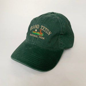 May include: A dark green baseball cap with an embroidered logo that reads "Grand Teton National Park" and features a deer silhouette.