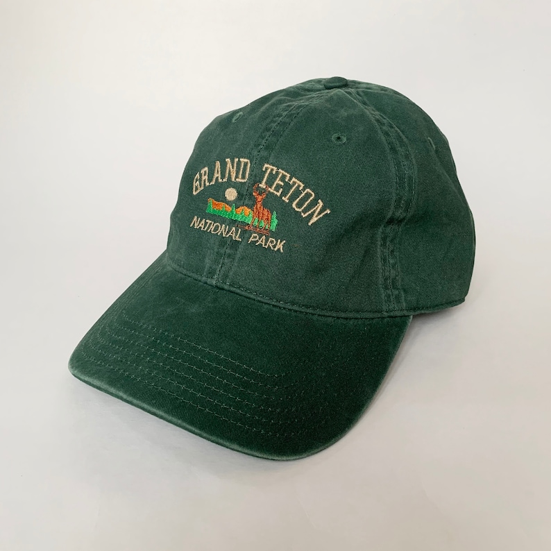 May include: A dark green baseball cap with an embroidered logo that reads "Grand Teton National Park" and features a deer silhouette.