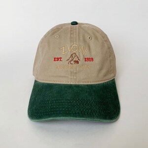 May include: A tan and green baseball cap with the text "Zion National Park Est. 1919" embroidered on the front.