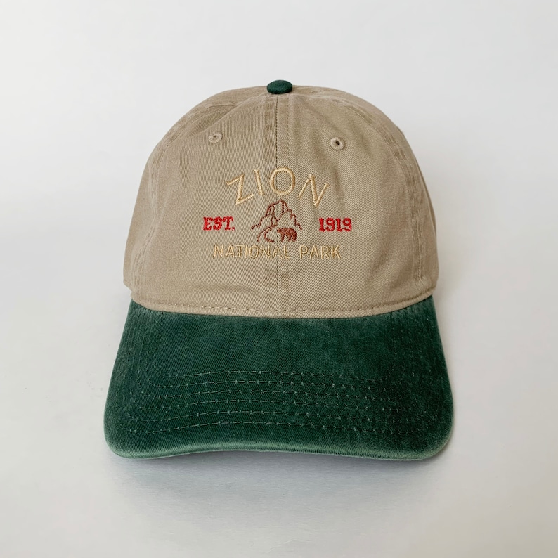 May include: A tan and green baseball cap with the text "Zion National Park Est. 1919" embroidered on the front.