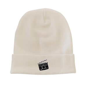 May include: White knit beanie with a black and white clapperboard design embroidered on the front.