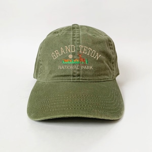 May include: A green baseball cap with an embroidered logo that says "Grand Teton National Park" with a deer and mountains in the design.
