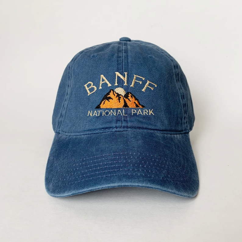 May include: A blue denim baseball cap with an embroidered logo that says "Banff National Park" with a mountain range and a sun graphic.