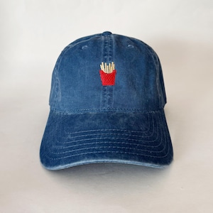 Könnte beinhalten: Eine blaue Baseballkappe aus Denim mit einem gestickten Bild eines roten Behälters mit Pommes Frites.