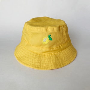 May include: A yellow bucket hat with an embroidered lemon design.