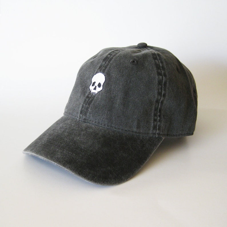 May include: A black, distressed, cotton baseball cap with a white embroidered skull design.