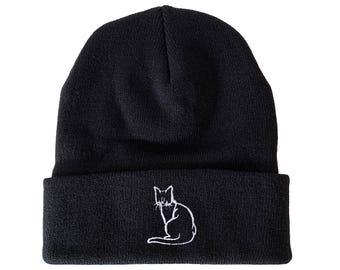 Puede incluir: Gorro negro con un diseño de gato bordado en blanco.