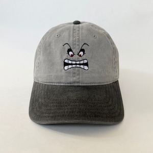 May include: A gray and black baseball cap with an embroidered angry face with red eyes.