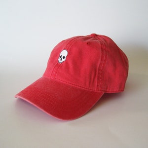 May include: A red baseball cap with a white skull embroidered on the front.