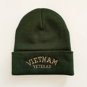 May include: A dark green knit beanie with the words "Vietnam Veteran" embroidered in gold on the front.