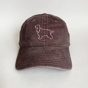 May include: A brown, distressed, cotton baseball cap with a white embroidered outline of a cocker spaniel.