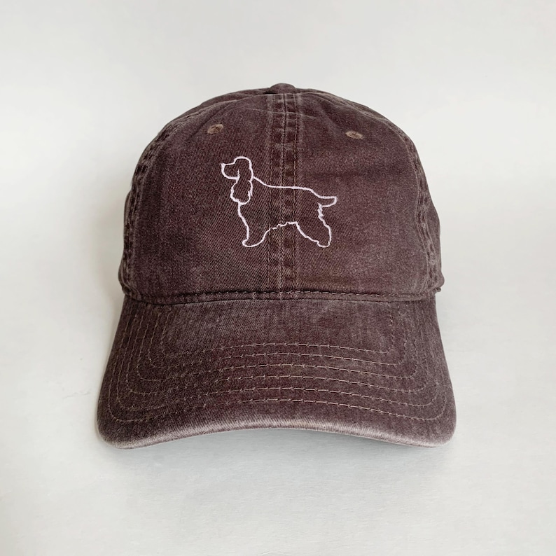 May include: A brown, distressed, cotton baseball cap with a white embroidered outline of a cocker spaniel.