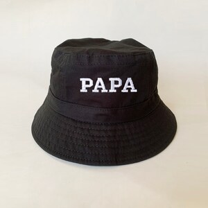 May include: Black bucket hat with the word "PAPA" embroidered in white on the front.