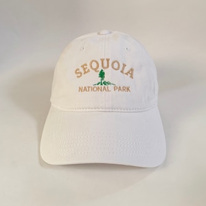 May include: White baseball cap with gold embroidery that reads "Sequoia National Park" with a green tree graphic.