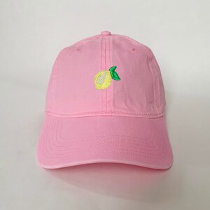 Pode incluir: Boné de beisebol rosa com aba curva. O boné apresenta um design de limão bordado na frente, com fruta amarela e folhas verdes. O boné é feito de um tecido macio e tem uma alça ajustável.