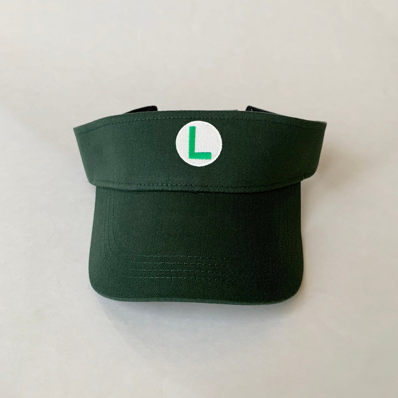 Op de afbeelding: Een donkergroene visor met een witte cirkel en een groene letter "L" in het midden.