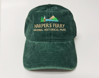 May include: A dark green baseball cap with the text "HARPERS FERRY NATIONAL HISTORICAL PARK" embroidered in gold. The cap features an embroidered design of a mountain, trees, and a building.