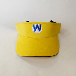 Op de afbeelding: Een gele visor met een zwarte rand en een blauwe en witte geborduurde "W" aan de voorkant.