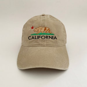 May include: A beige baseball cap with an embroidered California state flag design featuring a bear, a red star, and the word "CALIFORNIA".