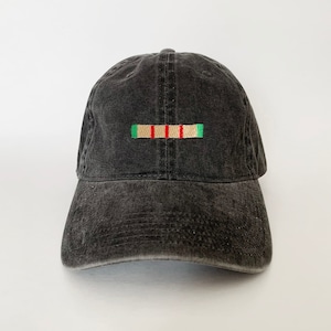 May include: A dark gray baseball cap with a curved brim. The cap features an embroidered design of a horizontal bar with red and green accents. The hat is made of a washed, textured fabric.