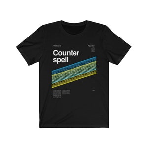 May include: Black t-shirt with a white graphic design that says "Counter spell" with a yellow and blue abstract design. The text "Third Level" and "Abjuration" are also on the shirt.