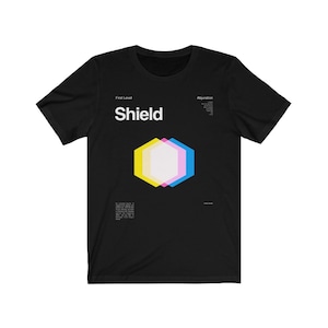 May include: Black t-shirt with a white graphic design of a shield with yellow, pink, and blue accents. The text "First Level" and "Shield" are printed in white above the graphic. The text "Abjuration" is printed in white on the right side of the graphic.