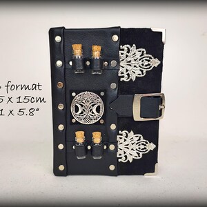May include: Black leather A6 format journal with silver accents. The journal features a decorative silver emblem, two small glass bottles with cork stoppers, and a black buckle closure. The dimensions are 4.1 x 5.8 inches.