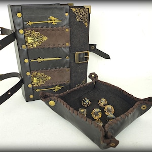 May include: A black and brown leather dice box and tray set. The box has decorative gold accents and straps. The tray is square with a stitched brown border. Several dice are in the tray.