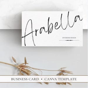 May include: A rectangular white business card template featuring the black handwritten script text Arabella and the words INTERIOR DESIGN below it. The card includes a decorative line element and the text BUSINESS CARD • CANVA TEMPLATE.