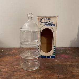 May include: A clear glass 4-piece Crystal Tower Set with a lid, three stacked compartments, and a cardboard box. The box has the words "4 PCE. Crystal TOWER SET" printed on it.