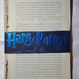 May include: A close-up of a book cover with the title "Harry Potter and the..." in a blue and silver font. The book cover features a blue background with a silver outline of a wizard's hat and a silver wand.
