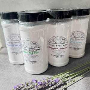 May include: Four clear plastic bottles filled with white carpet freshener powder, each topped with a black lid and a label reading Carpet Freshener with scents including White Sage and Lavender, Lemon and Basil, Mahogany Teakwood, and Fresh Linen.