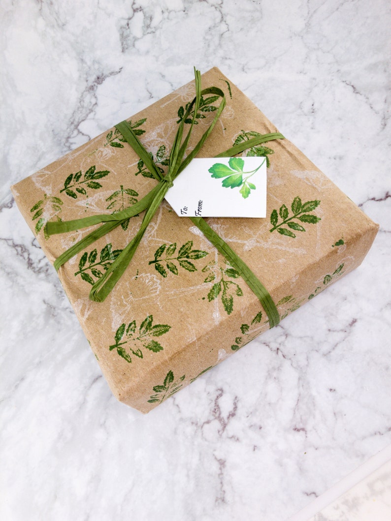 May include: A brown gift box wrapped in paper with a green leaf pattern. The box is tied with a green ribbon and has a white gift tag with the words "To" and "From" written on it.