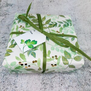 May include: A white gift box with a green ribbon and a green and gold floral pattern. The box has a white gift tag that says "To" and "From".