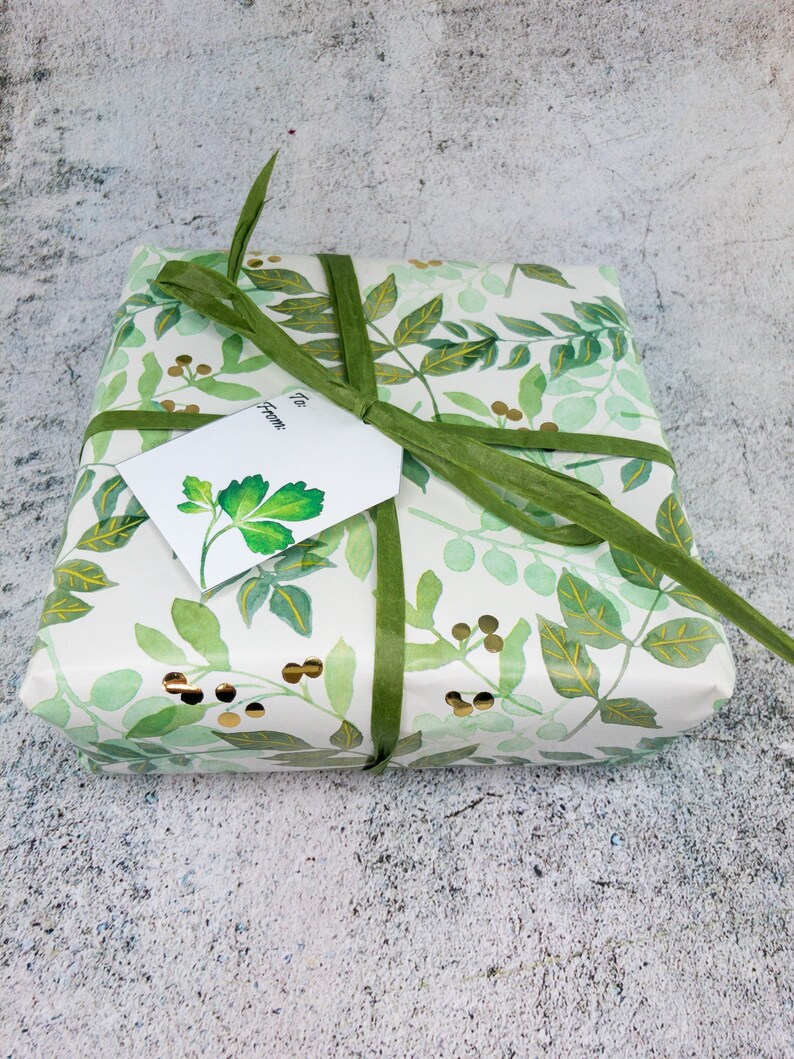 May include: A white gift box with a green ribbon and a green and gold floral pattern. The box has a white gift tag that says "To" and "From".