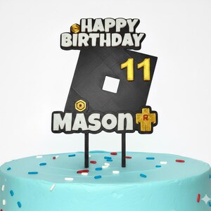 May include: A cake topper with the words "HAPPY BIRTHDAY" and the number "11" in gold. The name "MASON" is also displayed. The cake is light blue with colorful sprinkles.