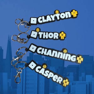 May include: Four keychains with names: "Clayton", "Thor", "Channing", and "Casper". Each keychain has a black base with white text and a yellow accent. The keychains are attached to silver keyrings and clasps.